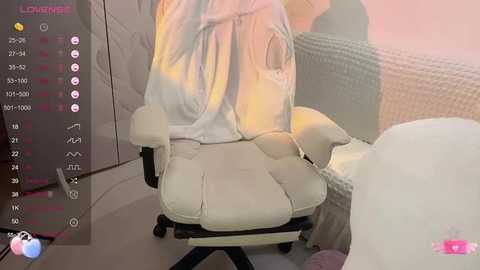 Media: Video of a white gaming chair with a white, wrinkled towel draped over it. The background features a light pink wall and a beige textured cushion.