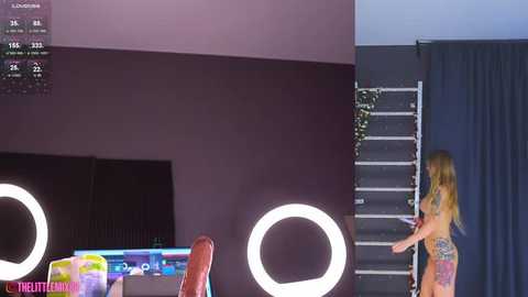 Media: Video of a modern, minimalist room with a young woman in a colorful bikini climbing a ladder next to a dark, circular mirror.