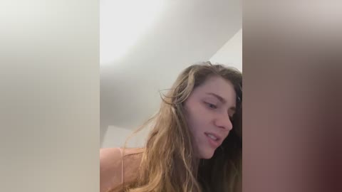 Media: Video of a young Caucasian woman with long, wavy blonde hair, wearing a light pink top, captured from a low angle, focusing on her face and shoulders.