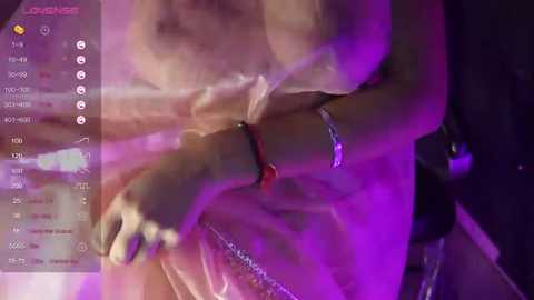 Media: A blurred, dimly lit close-up video of a woman in a sheer, translucent dress with a red bra visible, her arms crossed, set against a purple-hued background.