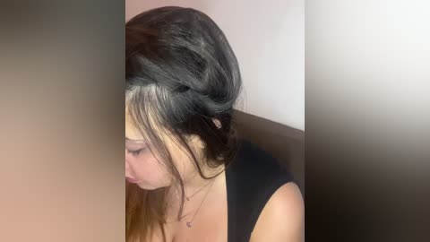 Media: Video of a young woman with medium-length, dark brown hair featuring a striking white streak, wearing a black top, looking downward.