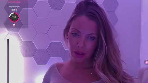 Media: Video of a blonde woman with wavy hair, wearing a white top, against a futuristic, hexagonal-patterned wall, with a digital overlay showing \"Hilltop\" and a 75% approval rating.