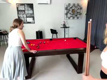 Media: Video of two women playing pool in a modern, minimalist room with a red pool table, black chairs, and abstract art on the walls.