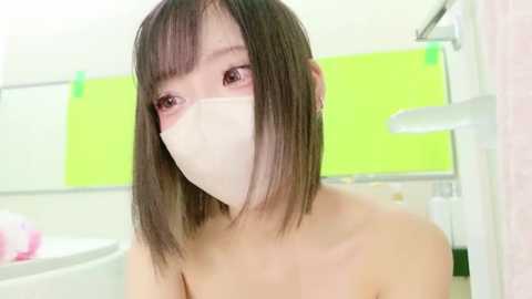 Media: Video of a young, fair-skinned Asian woman with straight, shoulder-length dark brown hair and bangs, wearing a white surgical mask, in a bright, modern bathroom with lime green walls and a white bathtub.