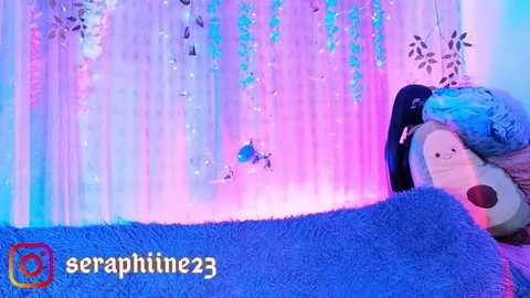 Media: A video of a soft, blue plush toy resting on a textured, blue blanket, against a backdrop of pastel-hued, glittery snowflakes and icicles, with a watermark reading \"seraphine23.\