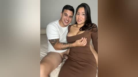 Media: Video of a smiling couple on a bed, man in white shirt, woman in brown dress, revealing tattooed arm and visible underwear.