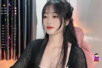 Media: Video of an East Asian woman with long black hair in a ponytail, wearing a black lace top and red lipstick. Background shows a pink chair and black curtains.