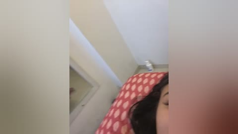 Media: A blurry video of a person's face, partially visible, with a red polka-dot pillow and white walls in the background, suggesting a bedroom setting.