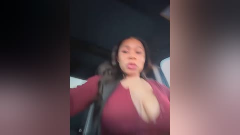 Media: Video of a curvaceous Black woman with medium skin tone and long black hair, wearing a low-cut red top that reveals ample cleavage, seated in a car with a dark interior.