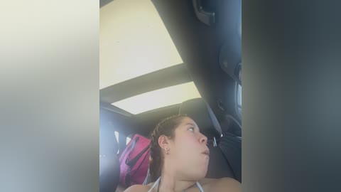 Media: A video of a young woman with light skin, brown hair, and a red backpack, sitting in a car, looking out the window.