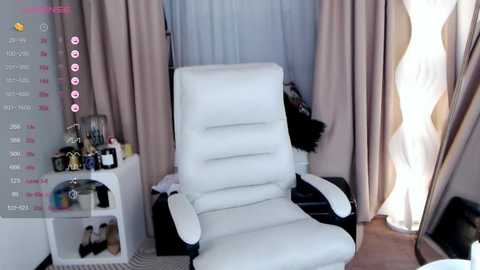 Media: Video of a modern, white leather recliner chair in a cozy, softly lit room with beige curtains, a side table, and a small white shelf.