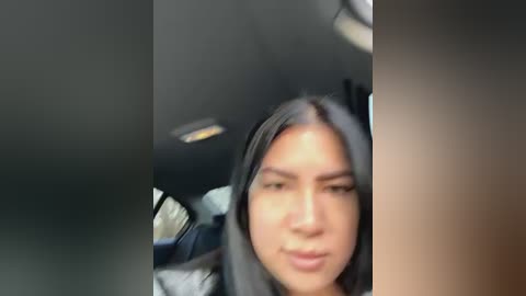 Media: A video captures a young woman with medium skin tone and long, dark hair inside a car, her face slightly out of focus. The background includes the car's interior and a blurred window.