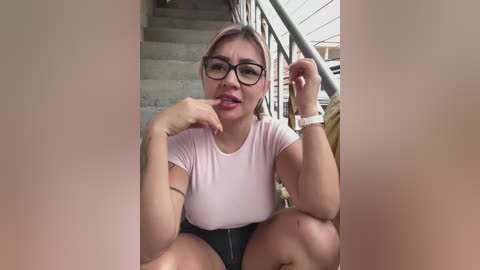 Media: A video of a young woman with light skin, glasses, and pink shirt, sitting on stairs, holding a piece of gum.