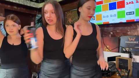 Media: Video of three young women in black tank tops, dancing energetically in a dimly lit bar with a colorful digital screen behind them.