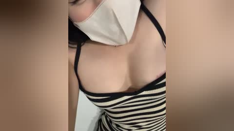 Media: A close-up video of a light-skinned woman with a white face mask, wearing a low-cut black and white striped dress that reveals cleavage, captured from above.