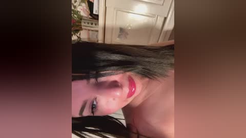 Media: A close-up video of a young woman with long, straight black hair, fair skin, and red lipstick, smiling seductively. She's in a kitchen with white cabinets and a blurred background.