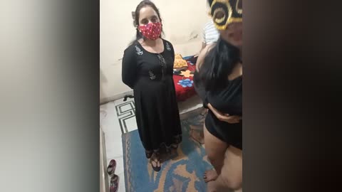 Media: Video of a pregnant woman in a black dress and red face mask, standing in a cluttered, dimly-lit room with a child and a partially visible person.