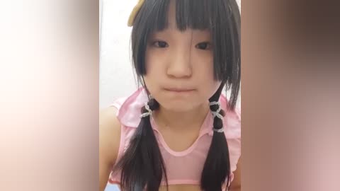 Media: A video of a young Asian girl with long black hair in twin braids, wearing a pink dress, looking serious and directly at the camera.