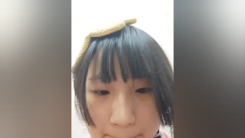 Media: A video of an Asian girl with black hair, wearing a pink floral dress, has a snake head resting on her forehead. The background is blurry and white.