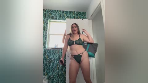 Media: Video of a plus-sized woman in green lingerie with a patterned background, standing in a narrow hallway. She has light skin and long brown hair.