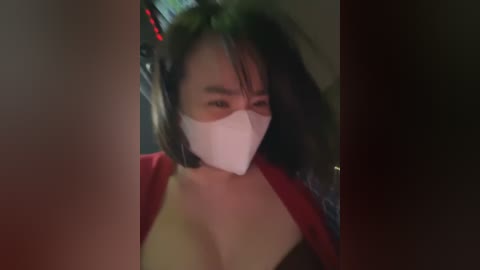 Media: Video of a woman with long black hair, wearing a white face mask, red top, and headphones, driving a car at night.