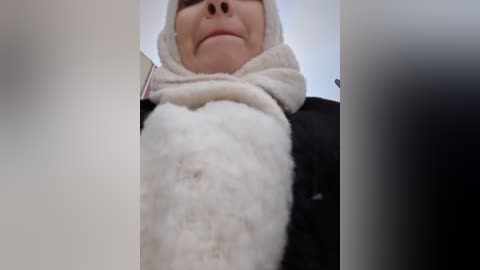 Media: Video of a person's face, partially obscured by a large white puff of cotton, wearing a black jacket and a beige headwrap, with a soft-focus background.