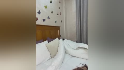 Media: Video of a cozy bedroom with a wooden headboard, white bedding, and a window partially covered by light gray curtains. The wall is adorned with butterfly decals in various colors, adding a whimsical touch.