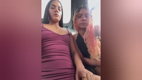 Media: Video of two women in a car: one with long black hair in a purple dress, the other with long pink-dyed hair in a black sleeveless top, sitting side-by-side.