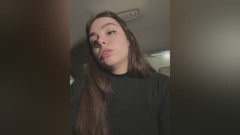 Media: A video of a young woman with long brown hair, wearing a black top, taking a selfie in a dimly lit car, with her head slightly tilted to the right.