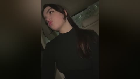 Media: A video of a young woman with long dark hair, wearing a black long-sleeve top, blowing a kiss towards the camera. The background is dimly lit with a hint of greenish-gray.