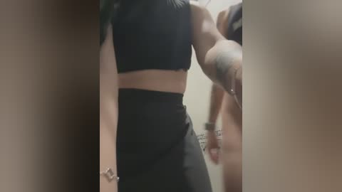 Media: Video of a woman in a black sports bra and high-waisted leggings, partially obscured by a doorway, showcasing toned arms and back, with a blurred background.