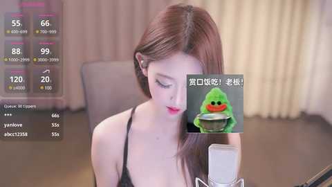 Media: A video of a fair-skinned woman with long brown hair, wearing a black spaghetti strap top, recording a video with a microphone. A green slime emoji is superimposed on the screen.