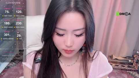 Media: A video of an East Asian woman with long black hair and fair skin, wearing a pink top, sitting indoors with a soft, pink background.