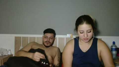 Media: Video of a Latino man with a mustache, shirtless, and a woman with a ponytail, both sleeping on a bed with a beige headboard and a water bottle.