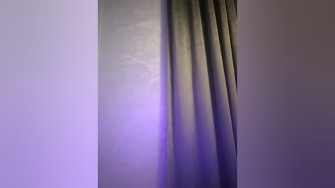 Media: A video of a plain, pale grey wall with a vertical line of dark, heavy curtains partially drawn, casting a shadow. The background is softly lit with a purple hue, creating a serene, minimalist atmosphere.