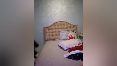 Media: Video of a messy bedroom with a beige headboard, a stuffed toy, and a bed with disheveled bedding and clothes.