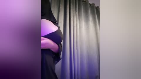 Media: Video of a woman in black lingerie, holding a soft toy, against gray curtains. Her fair skin and slender figure are partially visible. The lighting is soft, creating a sensual ambiance.