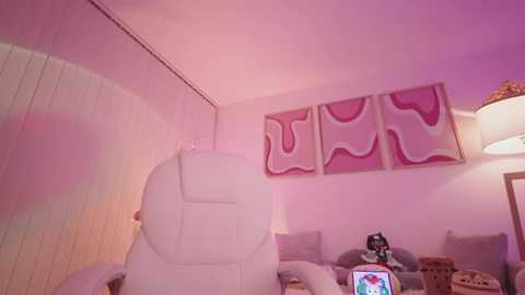 Media: Video of a cozy, pink-themed room with a white leather recliner, a console table, and a TV displaying a colorful game. Artwork and a lamp add ambiance.