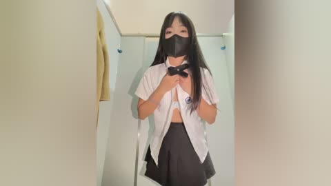 Media: Video of an Asian woman with long black hair, wearing a white blouse, black face mask, and black bow, posing in a dimly lit hallway.