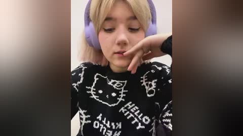 Media: A video of a young girl with blonde hair, wearing purple headphones and a black sweater with white text and a cat design, resting her chin on her hand.