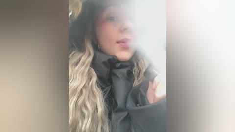 Media: Video of a blonde woman with fair skin, wearing a black hooded jacket and a black mask, partially obscured by fog, with a neutral expression.