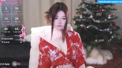 Media: Video of an Asian woman with fair skin and brown hair, wearing a red floral kimono, seated on a white couch in a festive room with a decorated Christmas tree.