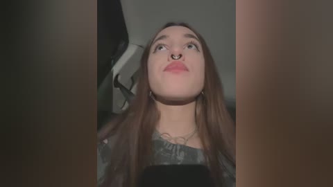 Media: Video of a young woman with long brown hair, wearing a black top and a nose ring, seated in a dimly lit car interior.