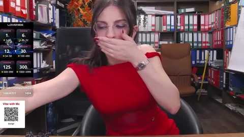 Media: A video of a woman in a red dress, covering her mouth, seated at a desk in an office with colorful bookshelves and a clock displaying 12:25.