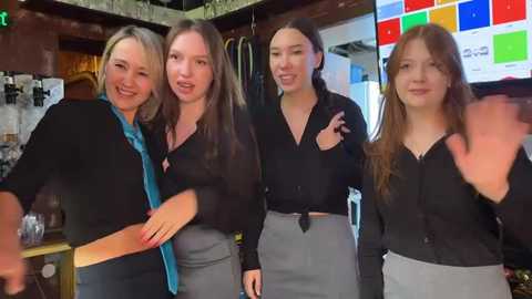 Media: Video of four women in a modern bar. Two women with short hair in black blazers and blue scarves; two women with long hair in black tops and grey skirts.