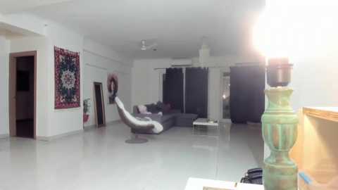 Media: Video of a modern, minimalist living room with a woman in a white dress and black shoes, standing near a grey couch and a colorful rug.