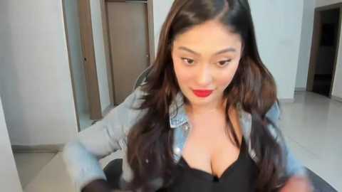 Media: A video of a young Asian woman with long black hair, wearing a denim jacket over a black bra, red lipstick, and seated indoors.