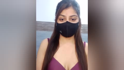 Media: Video of a young woman with long, straight dark hair, wearing a black face mask and a purple bralette, standing against a blurred lake and sky background.