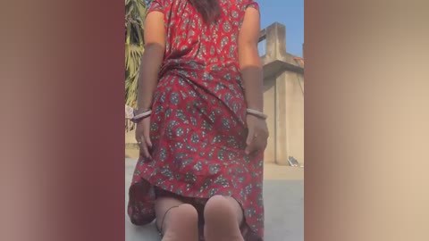 Media: Video of a woman in a red floral dress, bending over, with a tan complexion, wearing brown shoes, and a bracelet on her wrist.