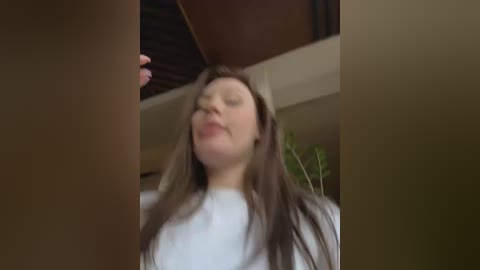 Media: A video shows a young woman with long brown hair, wearing a white shirt, caught mid-movement, with a blurred background suggesting a home interior.